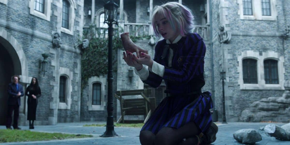 Enid Sinclair kneeling in a courtyard with Thing on Netflix's 'Wednesday' show
